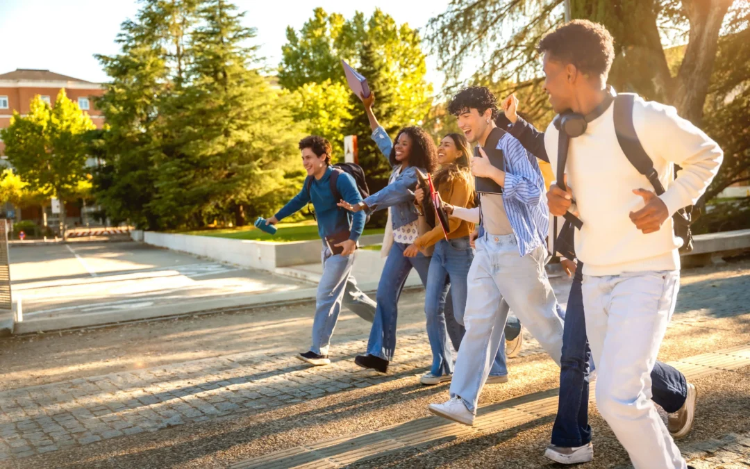 Group of diverse students walking quickly outdoors on a sunny campus, smiling and chatting with backpacks and notebooks.