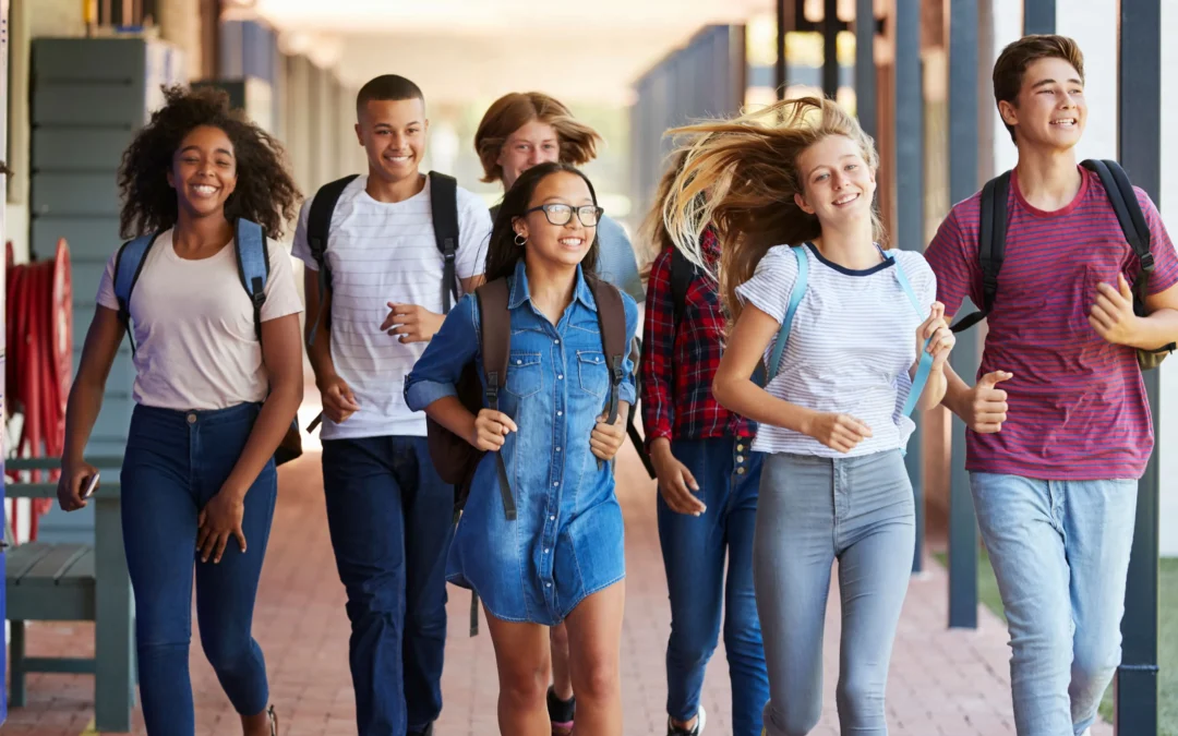 Group of smiling teenagers walking together with backpacks on a sunny school campus corridor