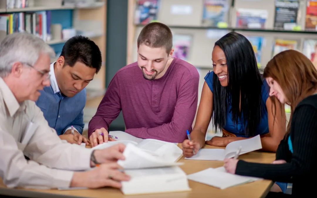 Group of five adults around a table collaborating on papers in a library or study room